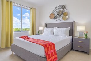Un dormitorio con cama, mesitas de noche, una obra de arte en la pared y una ventana con cortinas.