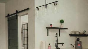 Una cucina con isola in legno, due sgabelli da bar in metallo, un rubinetto nero e una lampada a sospensione.