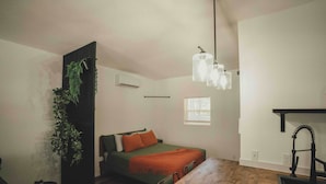 Una stanza accogliente e piccola con un letto, un tavolo da pranzo, una pianta pensile e una lampada a sospensione.