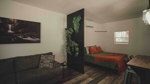 Una stanza con un divano, un letto, un tavolo da pranzo, una finestra e una pianta fissata al muro.
