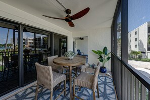 Ein Balkon mit Tisch und Stühlen, einem Deckenventilator und Blick auf das Meer und Gebäude.