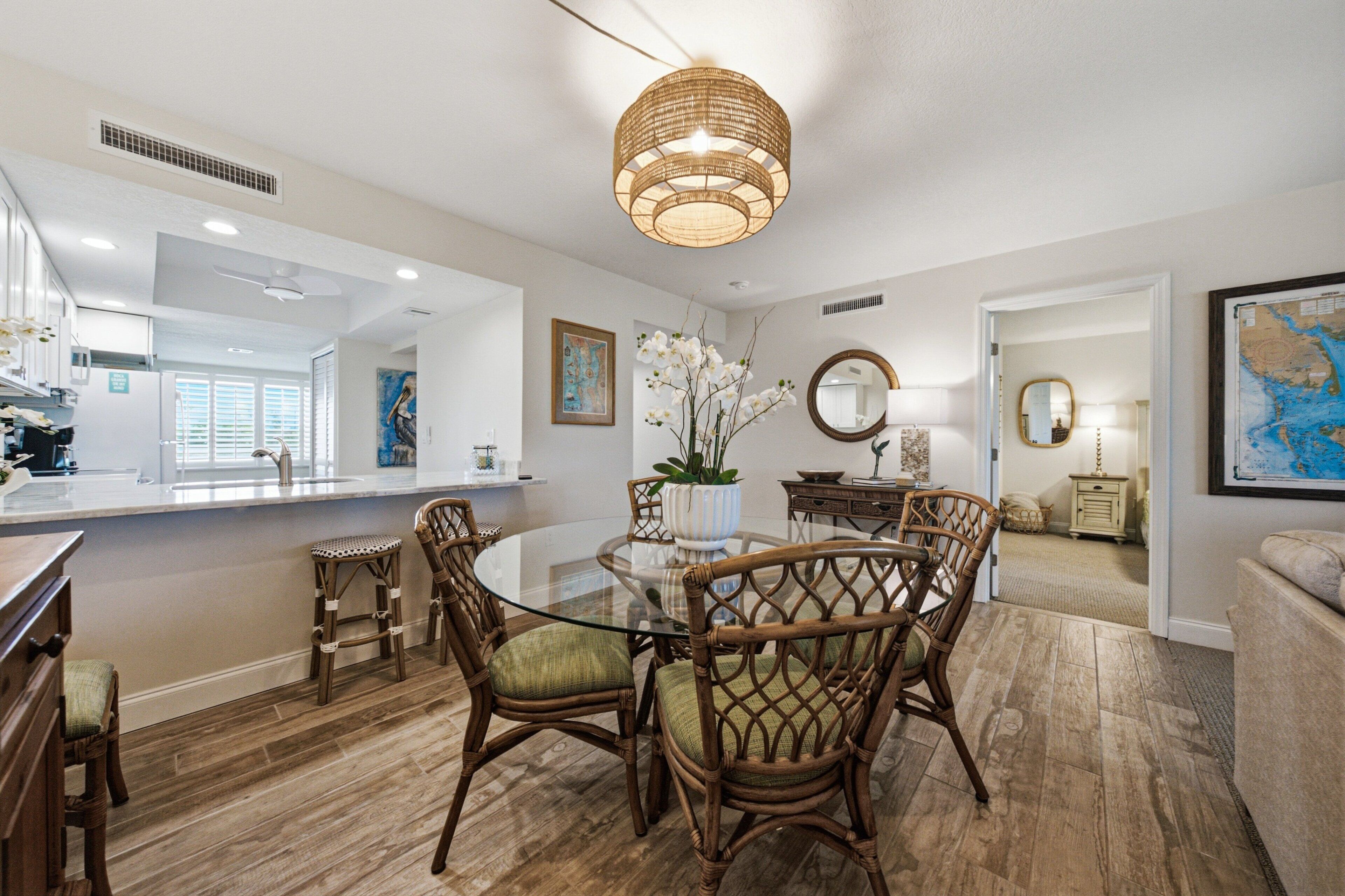 A dining area with a glass table, wicker chairs, and a hanging light fixture.