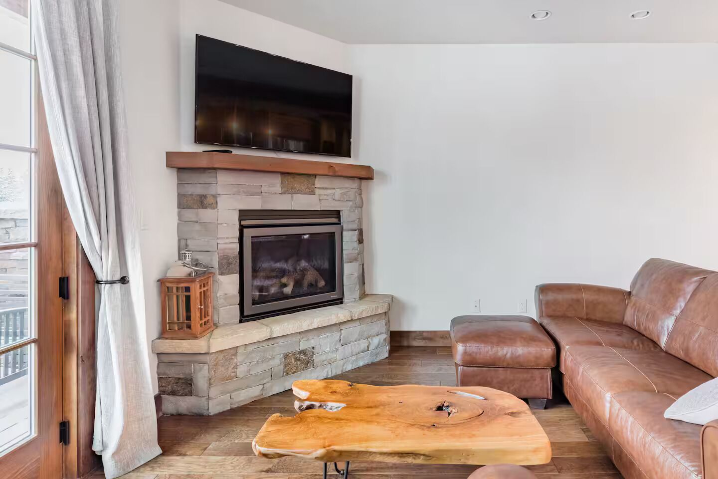 Una sala de estar con chimenea de piedra, sofá de cuero y mesa de centro de madera.