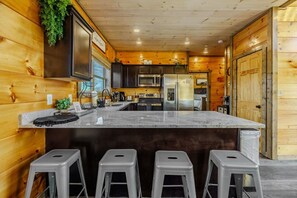 A modern kitchen with wooden walls, a marble island, and bar stools. - The Smokies Dream Lodge – Indoor Pool+Hot Tub & Epic Fun! (Sevierville)