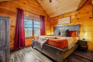 A wooden cabin bedroom with a bed, a nightstand, a window with curtains, and a sign on the wall. - The Smokies Dream Lodge – Indoor Pool+Hot Tub & Epic Fun! (Sevierville)