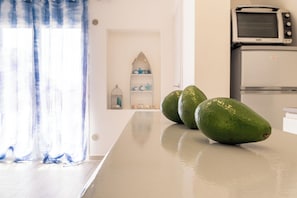 Eine Küche mit Mikrowelle und Kühlschrank, ein Fenster mit blauen Vorhängen und drei grüne Avocados auf einer Arbeitsplatte.