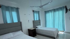 A hotel room with two beds, a ceiling fan, and a window with curtains.