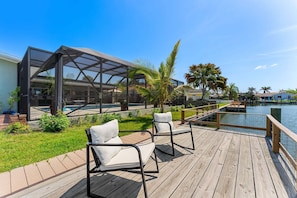 Eine Holzterrasse mit zwei weißen, gepolsterten Stühlen, einer gläsernen Struktur und einem Pool.