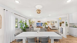 A modern living room with a dining area, white walls, and wooden flooring. - Tropical Cocoa Beach Riverfront Oasis | Pool, Hot Tub & Lanai 🍹🌴 (Cocoa Beach)