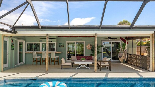 A covered outdoor swimming pool area with a glass roof, seating, and a dining area. - Tropical Cocoa Beach Riverfront Oasis | Pool, Hot Tub & Lanai 🍹🌴 (Cocoa Beach)