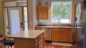 A kitchen with wooden cabinets, a stainless steel refrigerator, and a window with a view of trees. - Cozy 2-bedroom townhome in Eagle Crest with AC and gym access (Redmond)