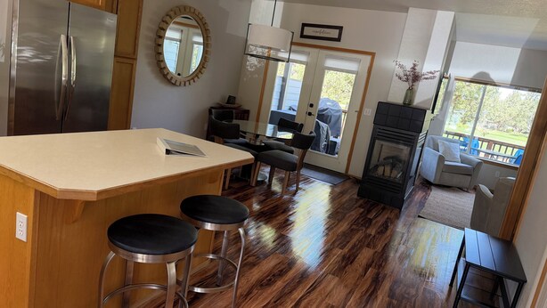 A kitchen with a large island, wooden cabinets, a stainless steel refrigerator, and a dining area with a table and chairs. - Cozy 2-bedroom townhome in Eagle Crest with AC and gym access (Redmond)