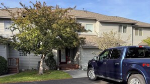 A residential driveway with a parked SUV, a house with a front porch, and a tree. - Cozy 2-bedroom townhome in Eagle Crest with AC and gym access (Redmond)