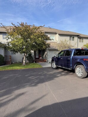 Eine Auffahrt mit einem geparkten SUV, ein Haus mit Veranda und ein Baum.