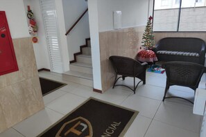 Eine Hotelhalle mit Empfangstresen, einem Weihnachtsbaum, Korbstühlen, einer Treppe und einem Fliesenboden.