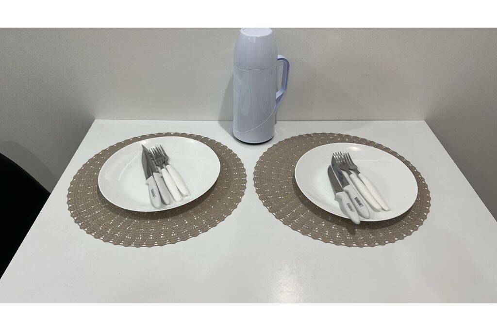 Two white plates with cutlery on a white table with a gray doily. A gray thermos is visible in the background.
