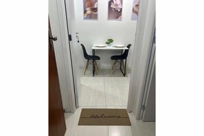 Ein Flur, der zu einem Essbereich mit Tisch und Stühlen führt, eine Fußmatte mit dem Schriftzug 'welcome' und gerahmte Bilder an der Wand.
