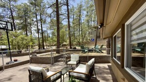 An outdoor patio with wicker furniture, a potted plant, and a view of a forested area. - Cozy Cabin Vibes- Hot Tub- Minutes to Downtown (Prescott)