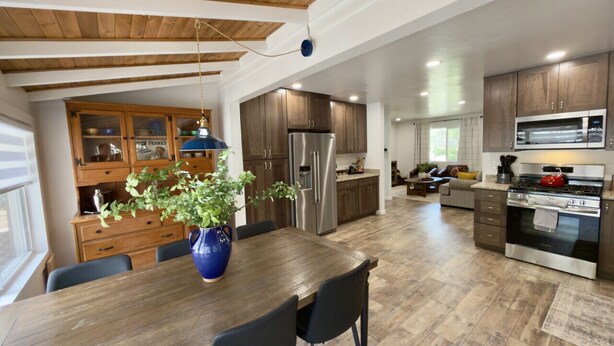 A modern kitchen with wooden cabinets, stainless steel appliances, and a dining area with a wooden table and chairs. - Cozy Cabin Vibes- Hot Tub- Minutes to Downtown (Prescott)