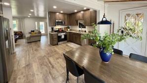 A spacious kitchen with wooden cabinets, a dining area with a table and chairs, and a living room with a sofa. - Cozy Cabin Vibes- Hot Tub- Minutes to Downtown (Prescott)