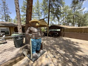 A bear statue with a hat and shorts, a trash can labeled 'City of Prescott,' and a covered area with a brick wall. - Cozy Cabin Vibes- Hot Tub- Minutes to Downtown (Prescott)