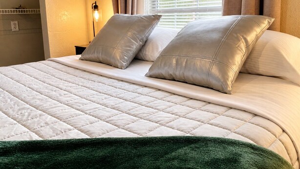 Un lit bien fait, avec une couette blanche matelassée, deux oreillers et un plaid vert.