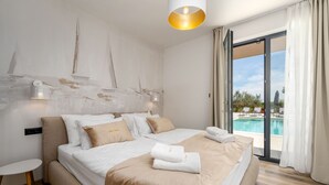 Quarto com cama, mesa de cabeceira, luminária, vista para piscina e porta de correr de vidro.