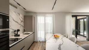 Uma cozinha moderna com bancada de mármore, forno embutido e área de jantar com mesa e cadeiras de mármore.