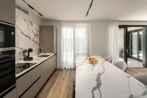 A modern kitchen with a marble countertop, a built-in oven, and a dining area with a marble table and chairs. - Villa Vanja (Istria - Poreč) (Poreč)