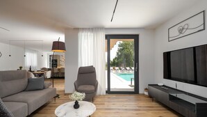 Uma sala de estar moderna com sofá, poltrona, televisão e mesa de centro de vidro.