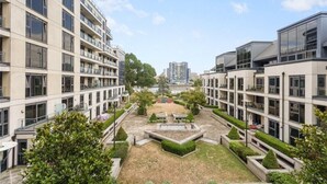 Un moderno complejo de apartamentos con varios pisos, balcones y un patio central con vegetación.