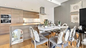 Una cocina moderna con electrodomésticos integrados, un comedor con mesa de vidrio y una sala de estar con televisor de pantalla plana.