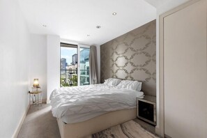 Ein modernes Schlafzimmer mit einem großen Bett, einem Nachttisch, einem Spiegel und Blick auf die Stadt.