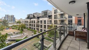 Un edificio moderno con balcón, barandillas de vidrio y vista a otros edificios.