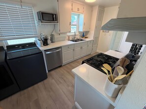 A compact kitchen with a dishwasher, microwave, stove, and a window with blinds.