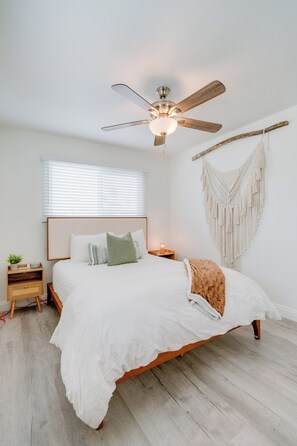 Une chambre à coucher avec un lit, un ventilateur de plafond, une décoration murale en macramé et une table de chevet avec une lampe.