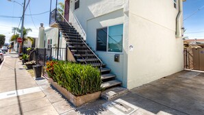 Un edificio de dos pisos con una escalera visible, un pequeño balcón y una jardinera con plantas.
