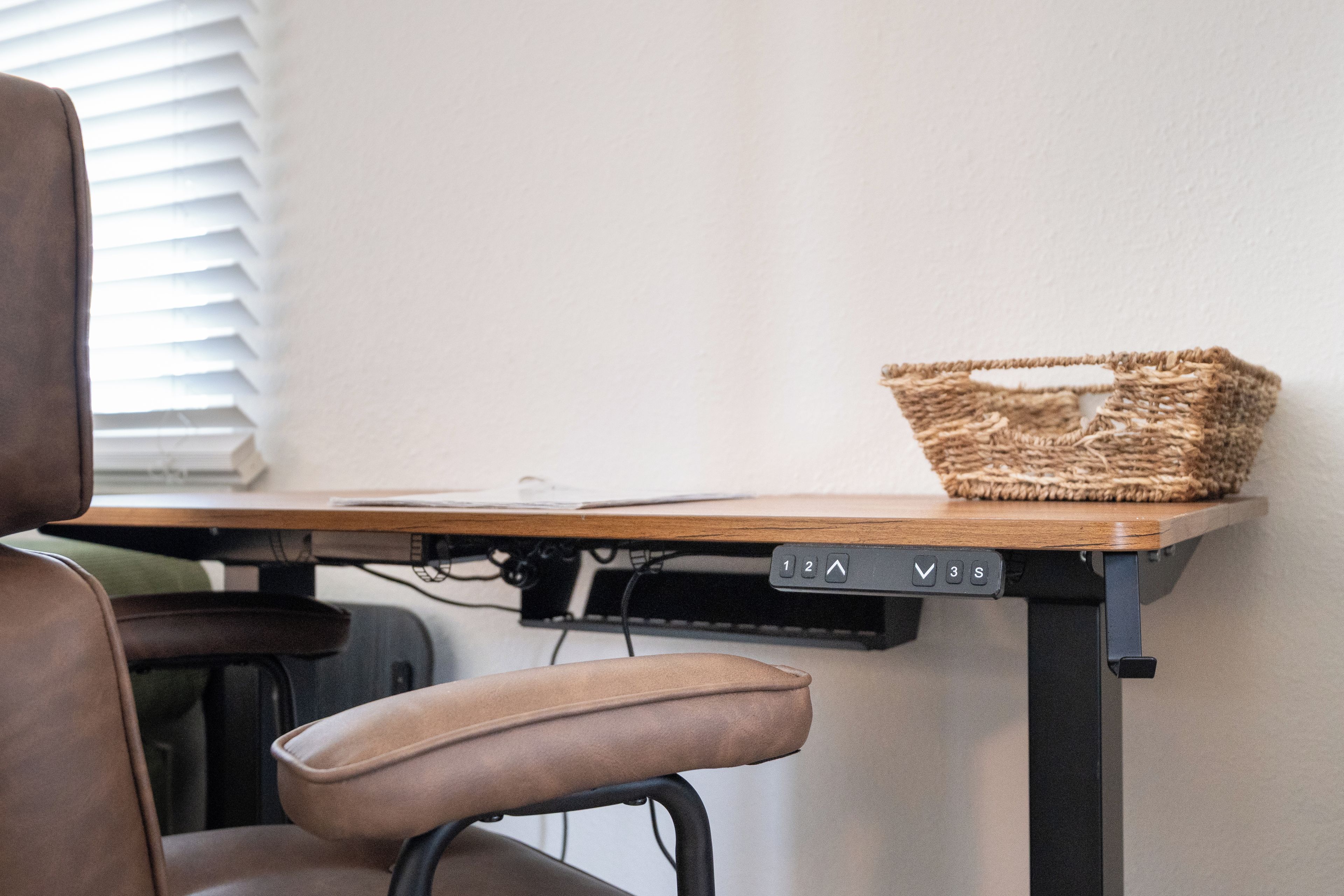 A desk with a woven basket, a chair, and a wall-mounted control panel.