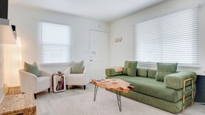 Una sala de estar con un sofá verde, sillones blancos y una mesa de centro de madera.