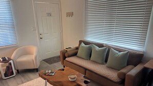 Una sala de estar con un sofá marrón, una mesa de centro de madera, un sillón blanco y una puerta con un letrero.