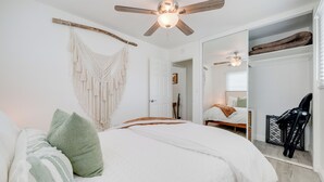 Un dormitorio con una cama, un ventilador de techo, un tapiz de macramé y un espejo grande.