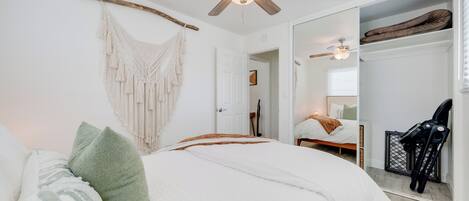 A bedroom with a bed, a ceiling fan, a macrame wall hanging, and a large mirror.