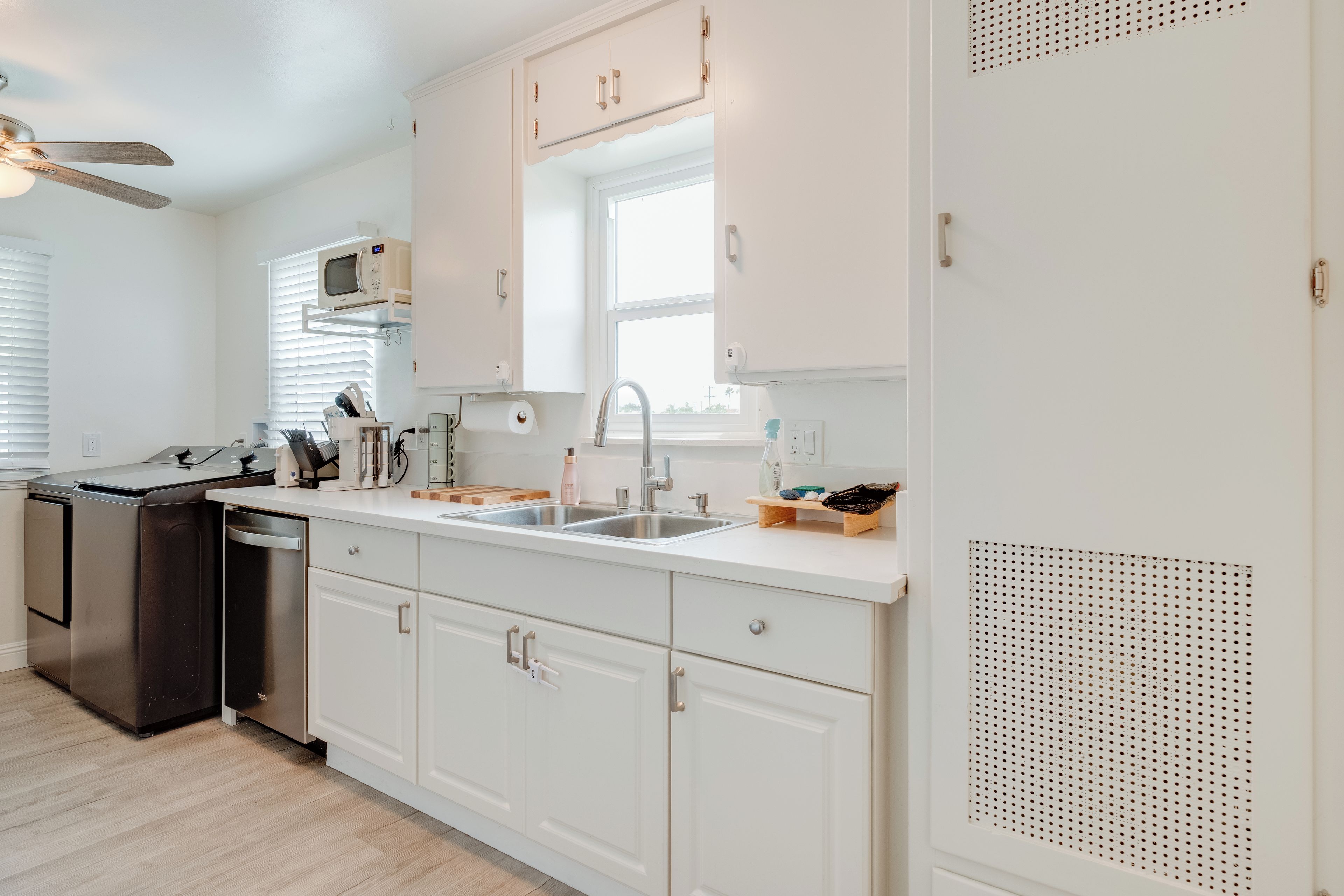 Una cocina moderna con armarios blancos, microondas integrado, lavavajillas y refrigerador de acero inoxidable.