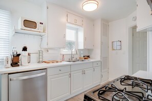 Une cuisine moderne avec des meubles blancs, un four à micro-ondes encastré, une cuisinière à gaz et une fenêtre au-dessus de l’évier.