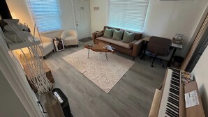 Una sala de estar con sofá, sillón, mesa de centro y un piano.