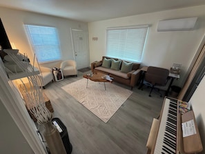A living room with a sofa, armchair, coffee table, and a piano.