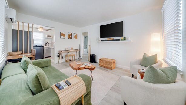 Una sala moderna con sofá, mesa de centro, televisor y una cocina al fondo.