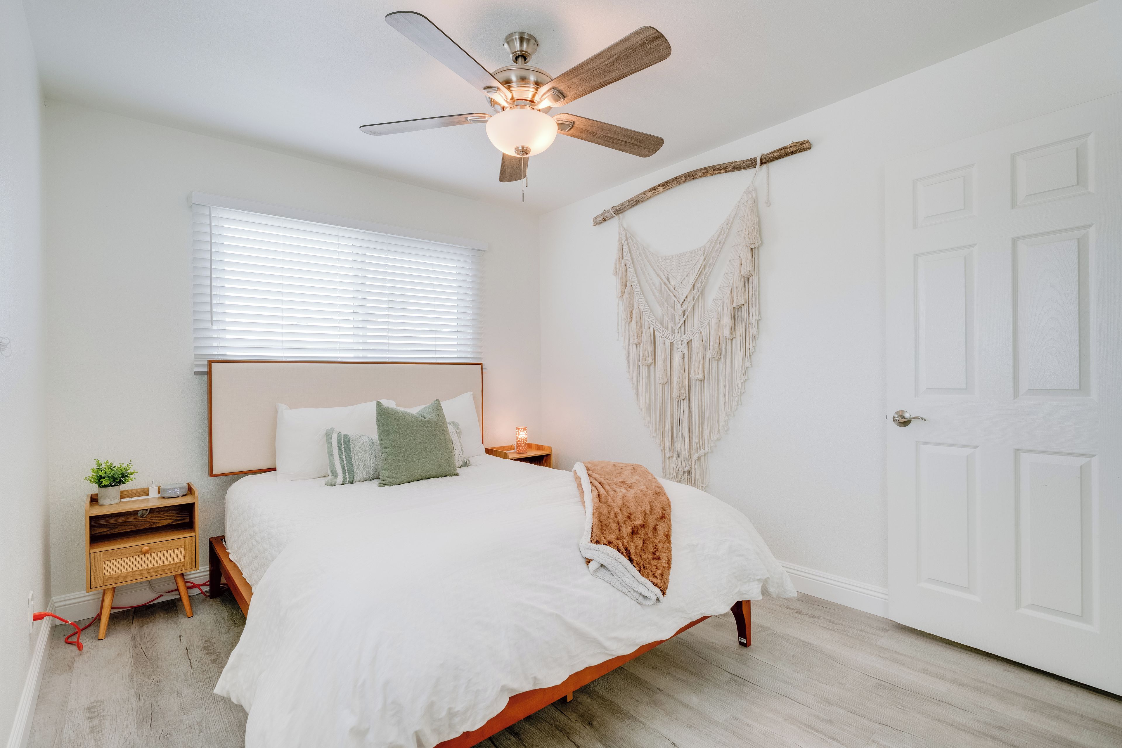 Un dormitorio con cama, mesita de noche, un tapiz de macramé en la pared y un ventilador de techo.