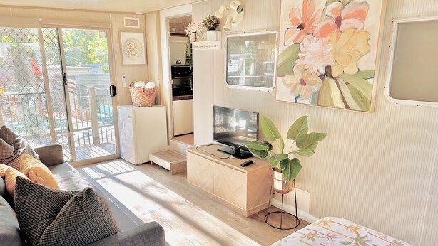 A compact living space with a sofa, a TV, a small kitchen area, and a sliding glass door leading to an outdoor area. - Elizabeth the spacious retro caravan. Sleeps 6 | Rye, Mornington Peninsula (Rye)