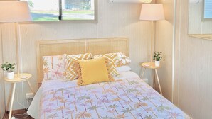 A bedroom with a bed, two bedside tables with lamps, a window, and an air conditioning unit. - Elizabeth the spacious retro caravan. Sleeps 6 | Rye, Mornington Peninsula (Rye)